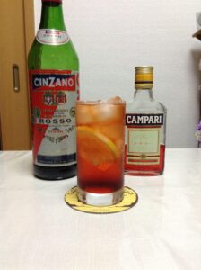 氷を入れたグラスに注がれた、鮮やかな赤色のアメリカーノ。レモンピールを添えた一杯