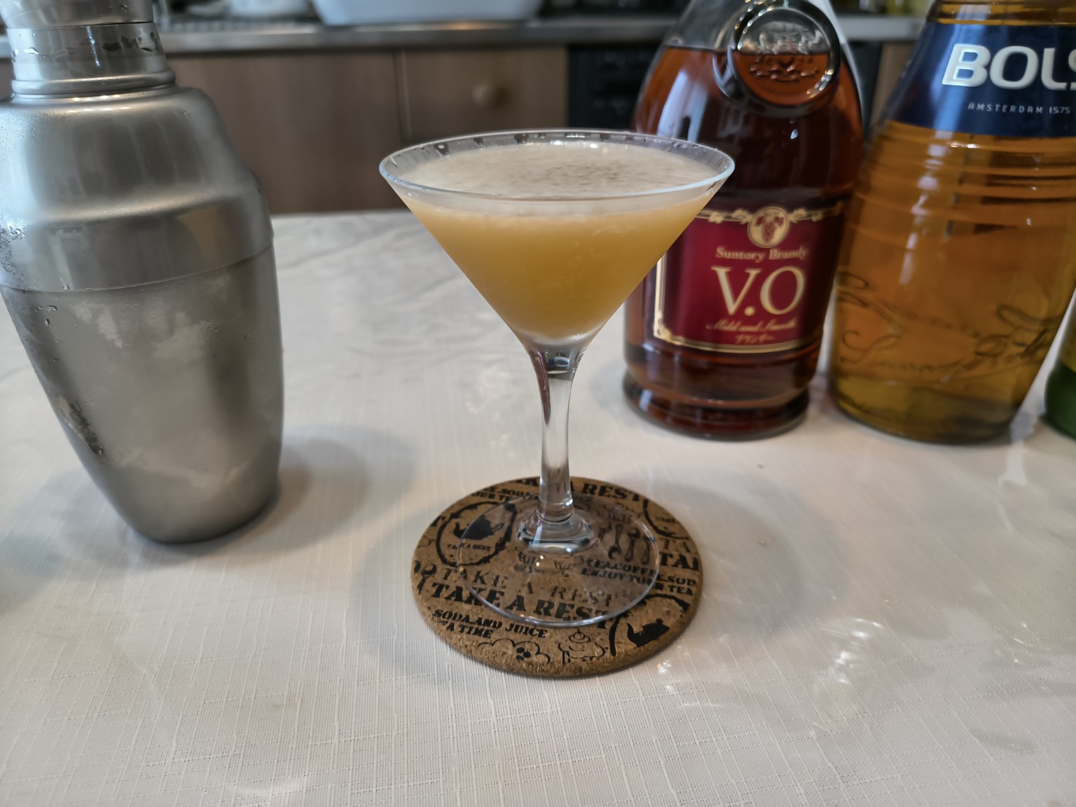 カクテルグラスに注がれたキューバン・カクテル。サントリー ブランデー V.OとBOLS アプリコット・ブランデーが背景に写る。